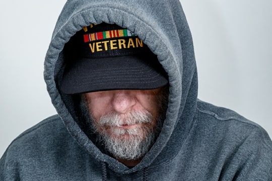 A Vietnam War USA military veteran is looking down with his partially obscured face showing a serious facial expression.