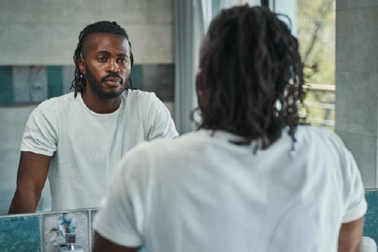Man looking at his reflection in wall-mounted mirror.