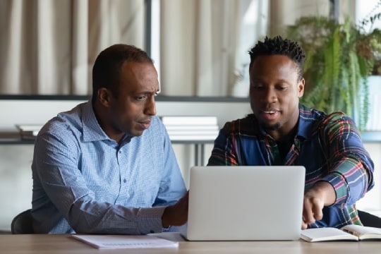 Two employees working on project together, using a laptop and pointing at the screen.